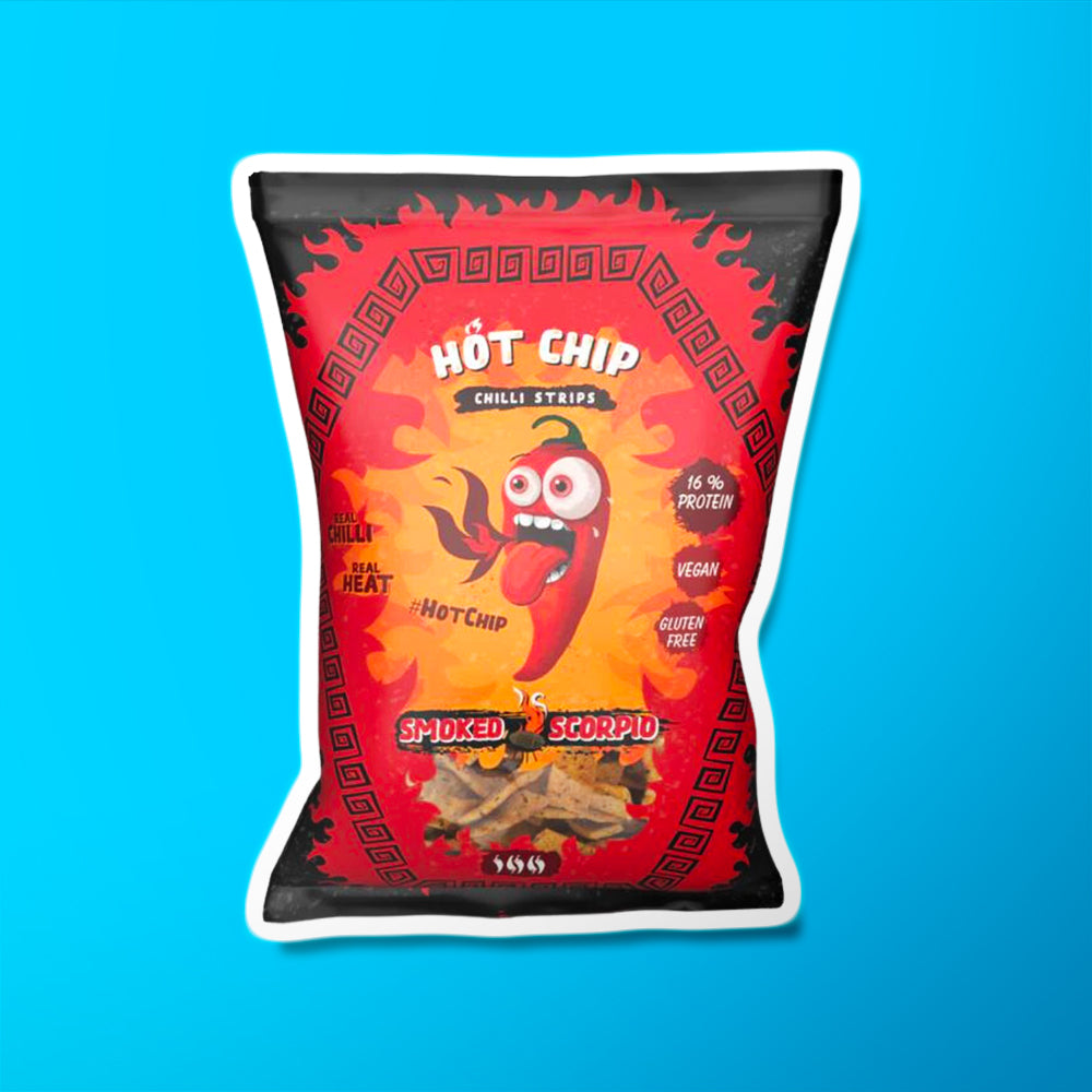 Un emballage rouge et noir sur fond bleu avec au centre un piment avec des yeux écarquillés et une bouche qui crache du feu. En bas, il y a une partie transparente avec des petits chips de forme rectangulaires